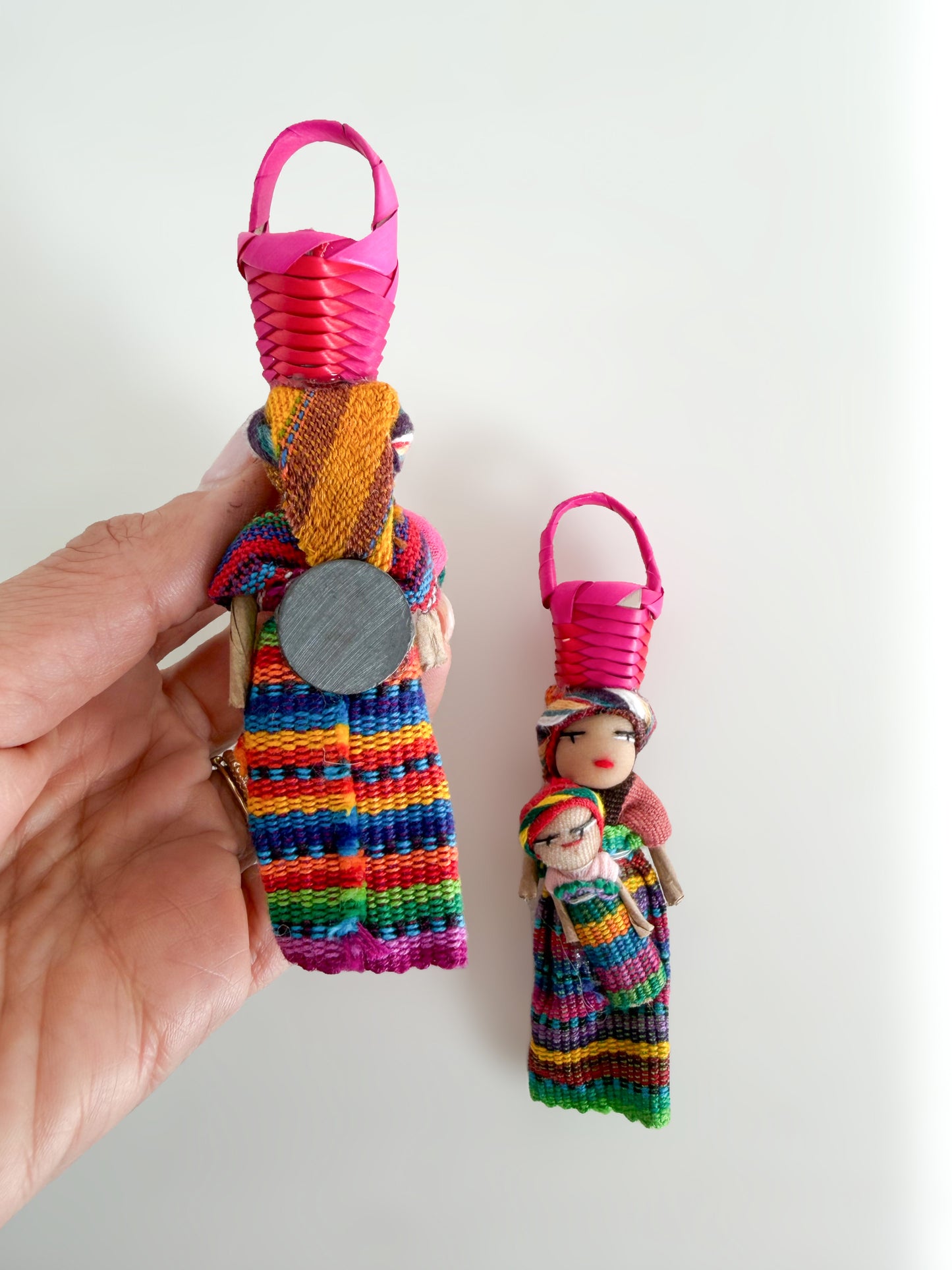 Colorful woven worry doll magnet with a small figurine held by a hand 