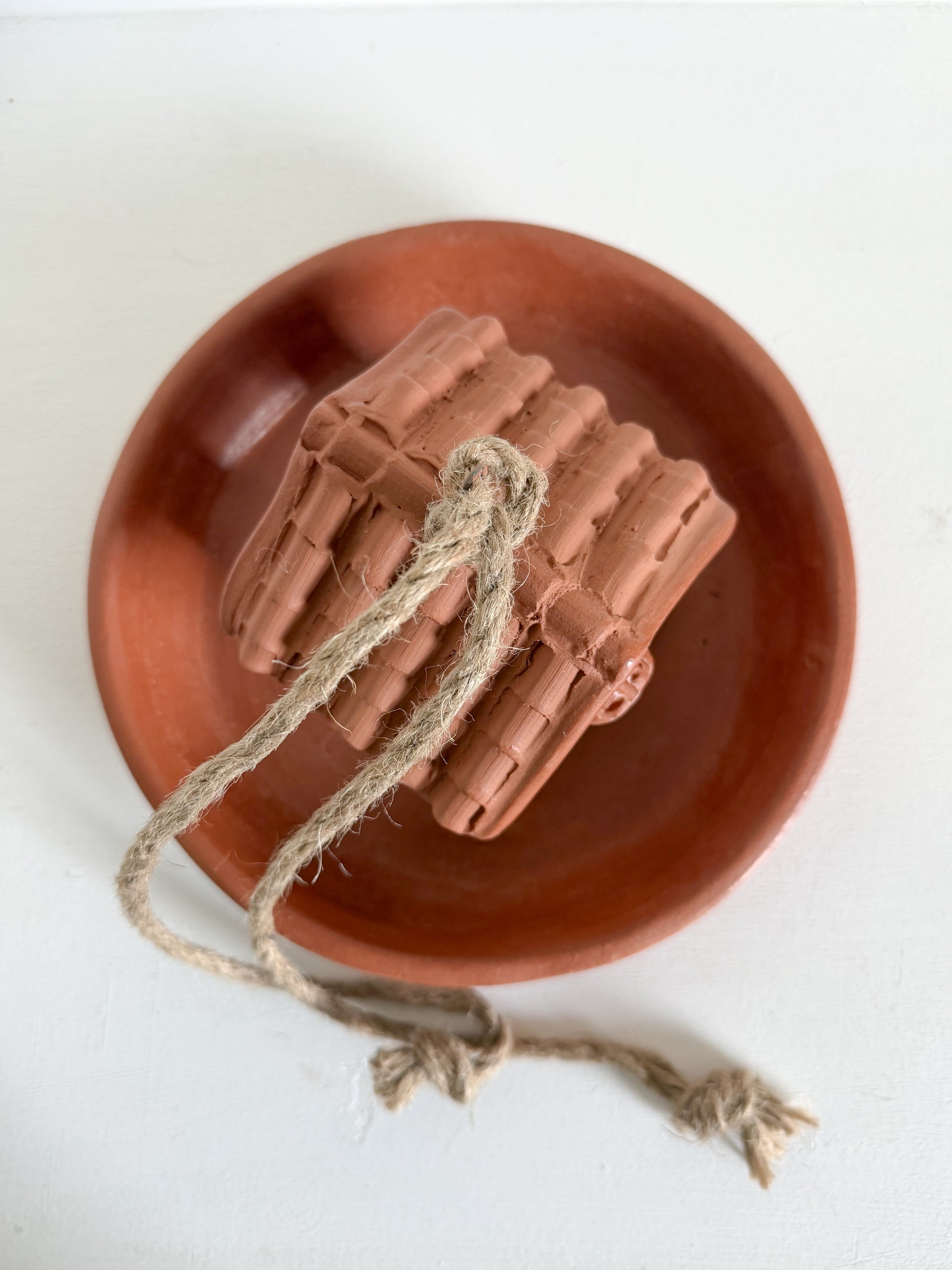A terracotta-colored clay miniature set of hand drums with a natural jute rope, displayed on a matching round terracotta plate against a clean white background.